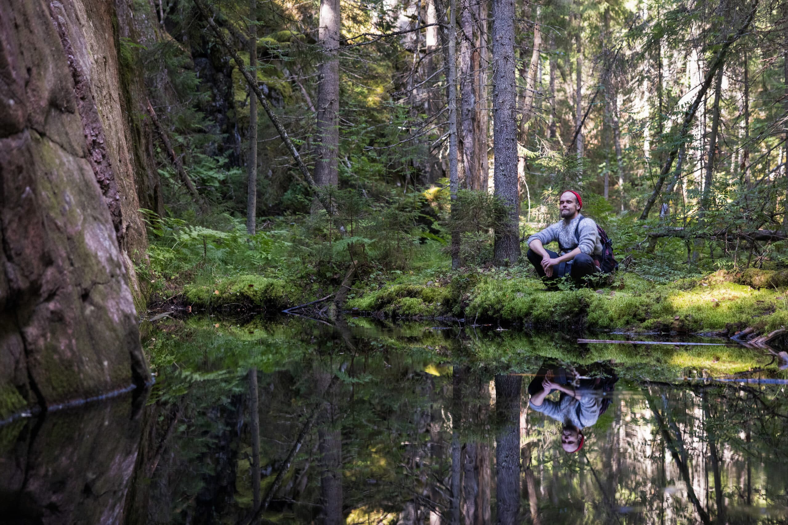 Retkeilijä istuu lammen rannalla Synninlukon luontokohteessa