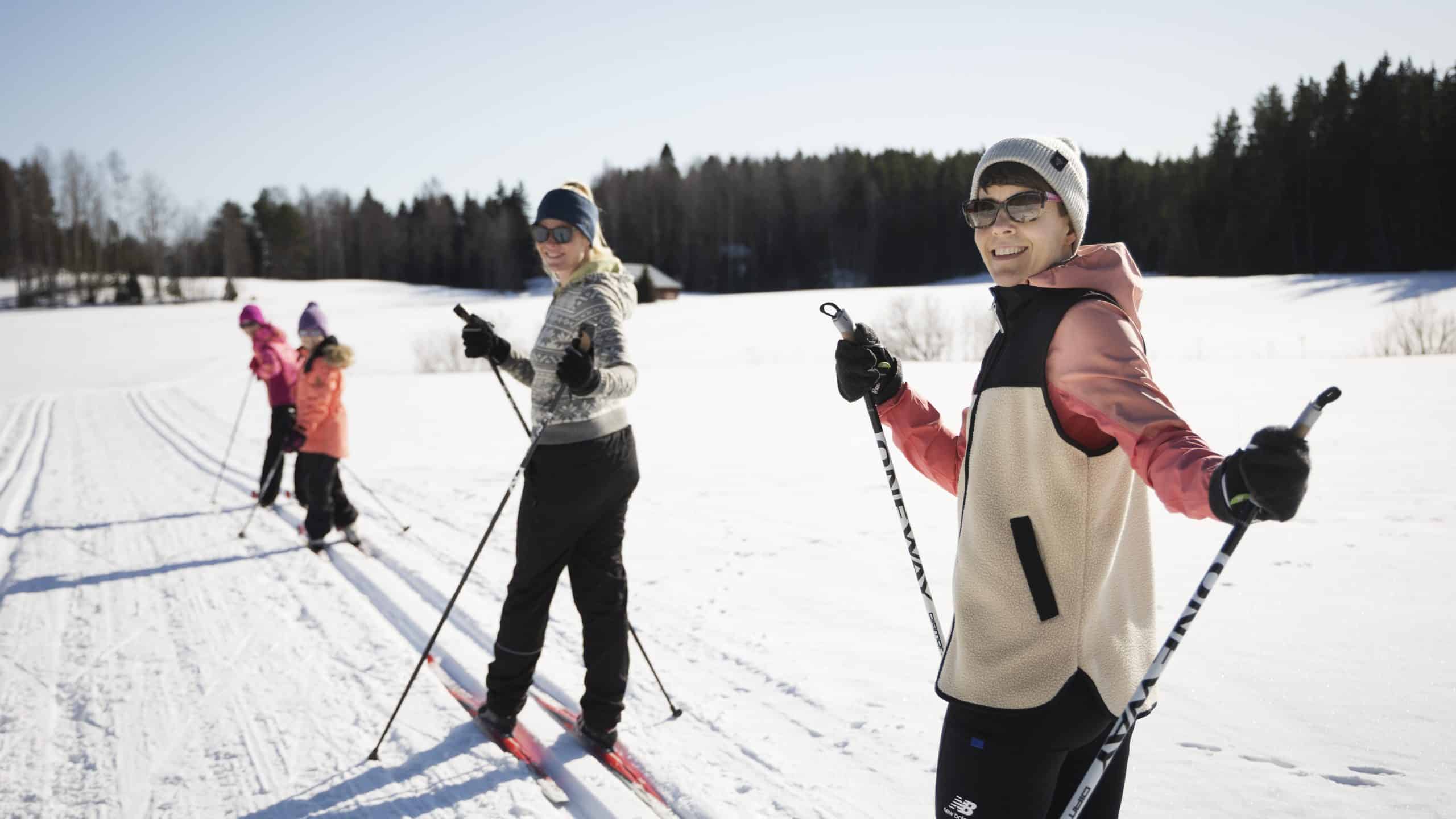 Hiihtäjät peräkkäin ladulla katsoo kameraan