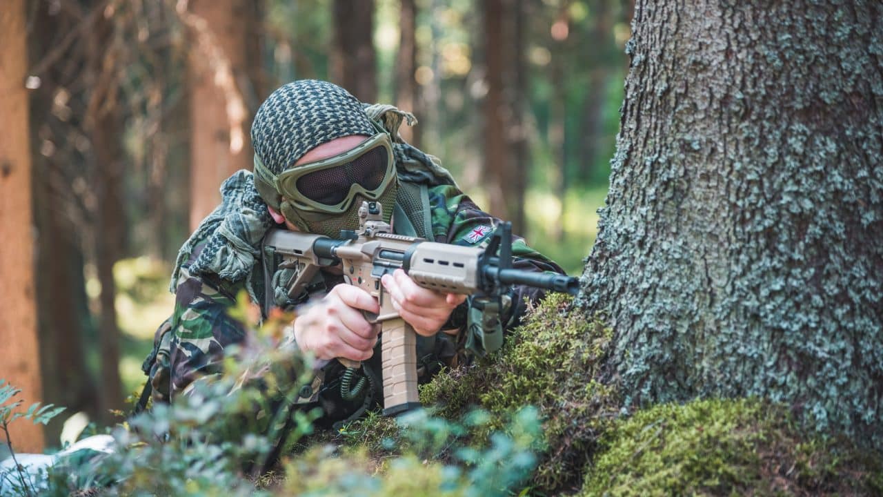 Airsoft-pelaaja tähtää puun takana suojassa