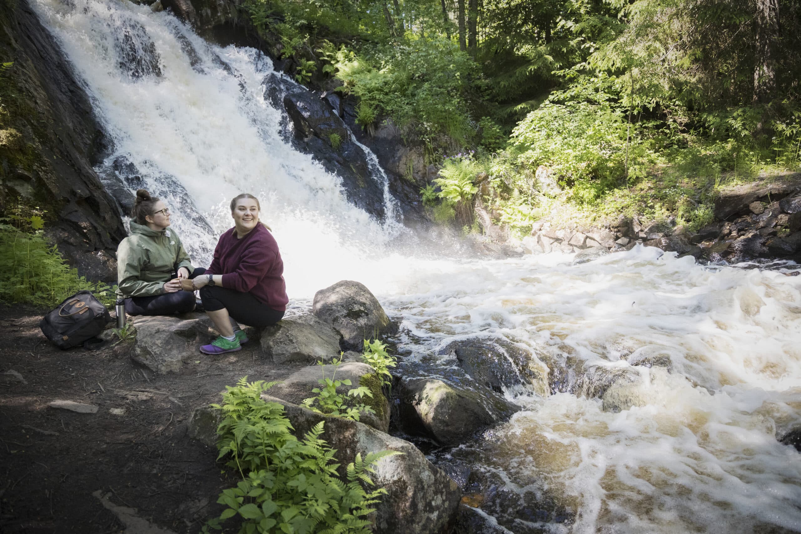Kaksi naista istuu Juveninkoskella kuohuvan vesiputouksen äärellä