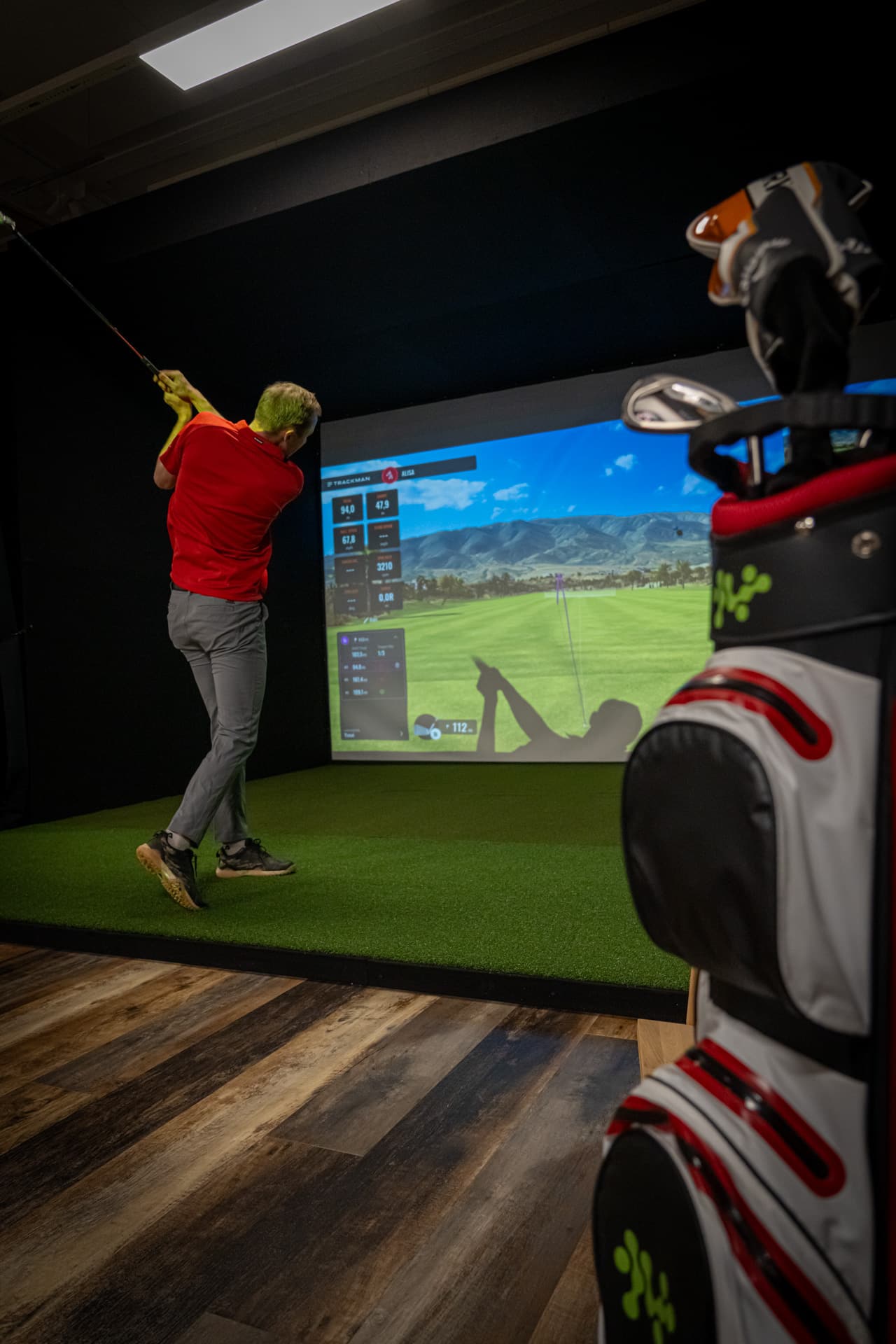 Henkilö lyö golf-palloa simulaattorissa.