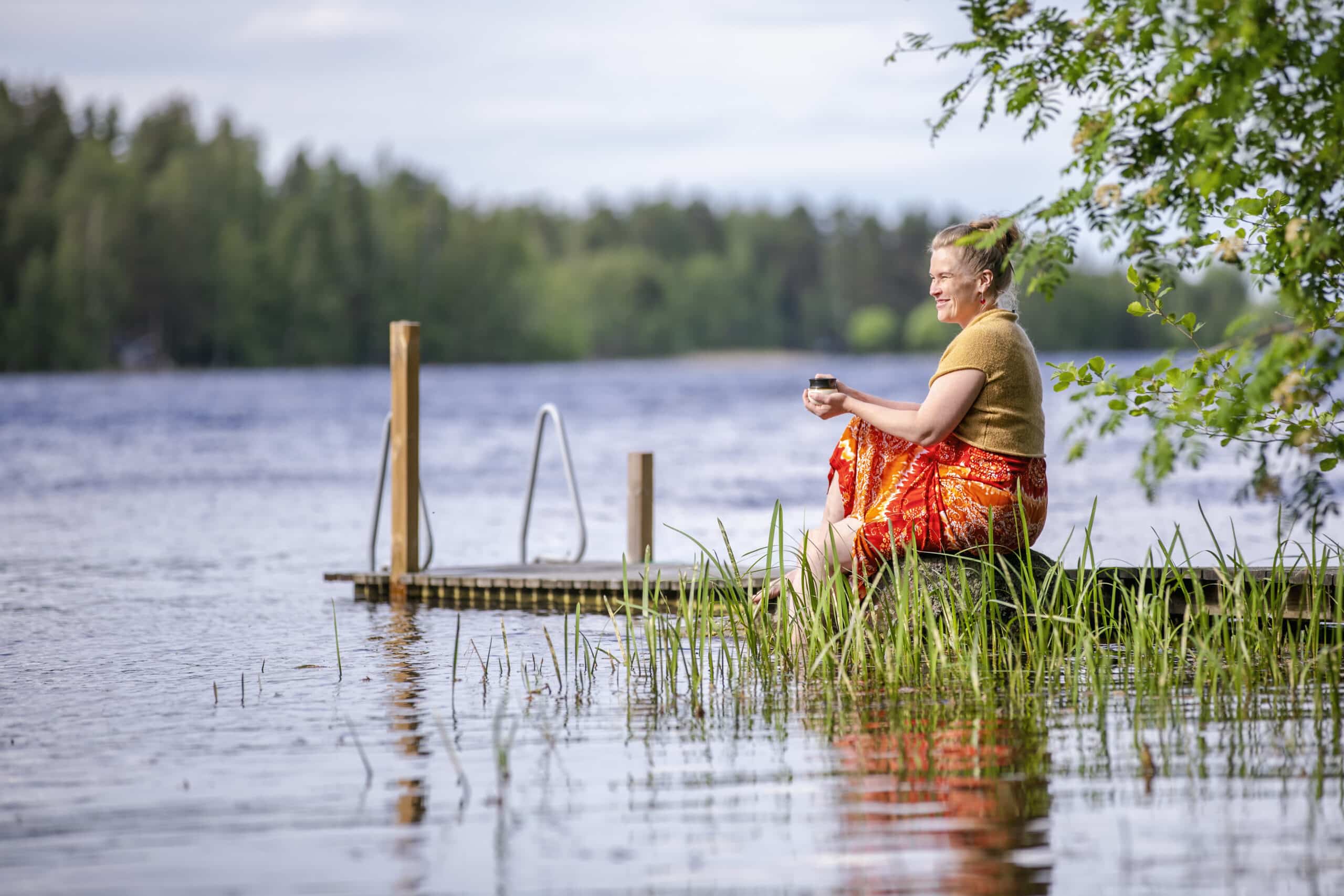 Nainen juo kahvia laiturilla kesällä.