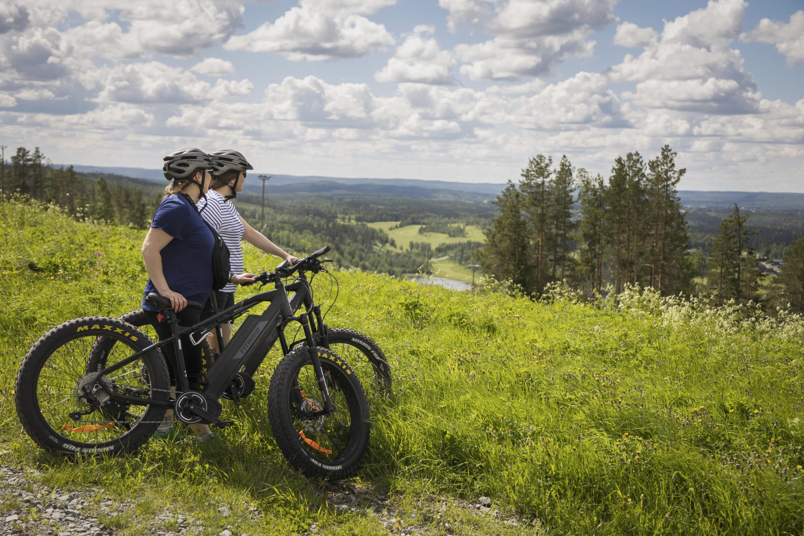 Fatbiket ja kaksi naista, jotka ihailevat maisemia Himoksen huipulla.