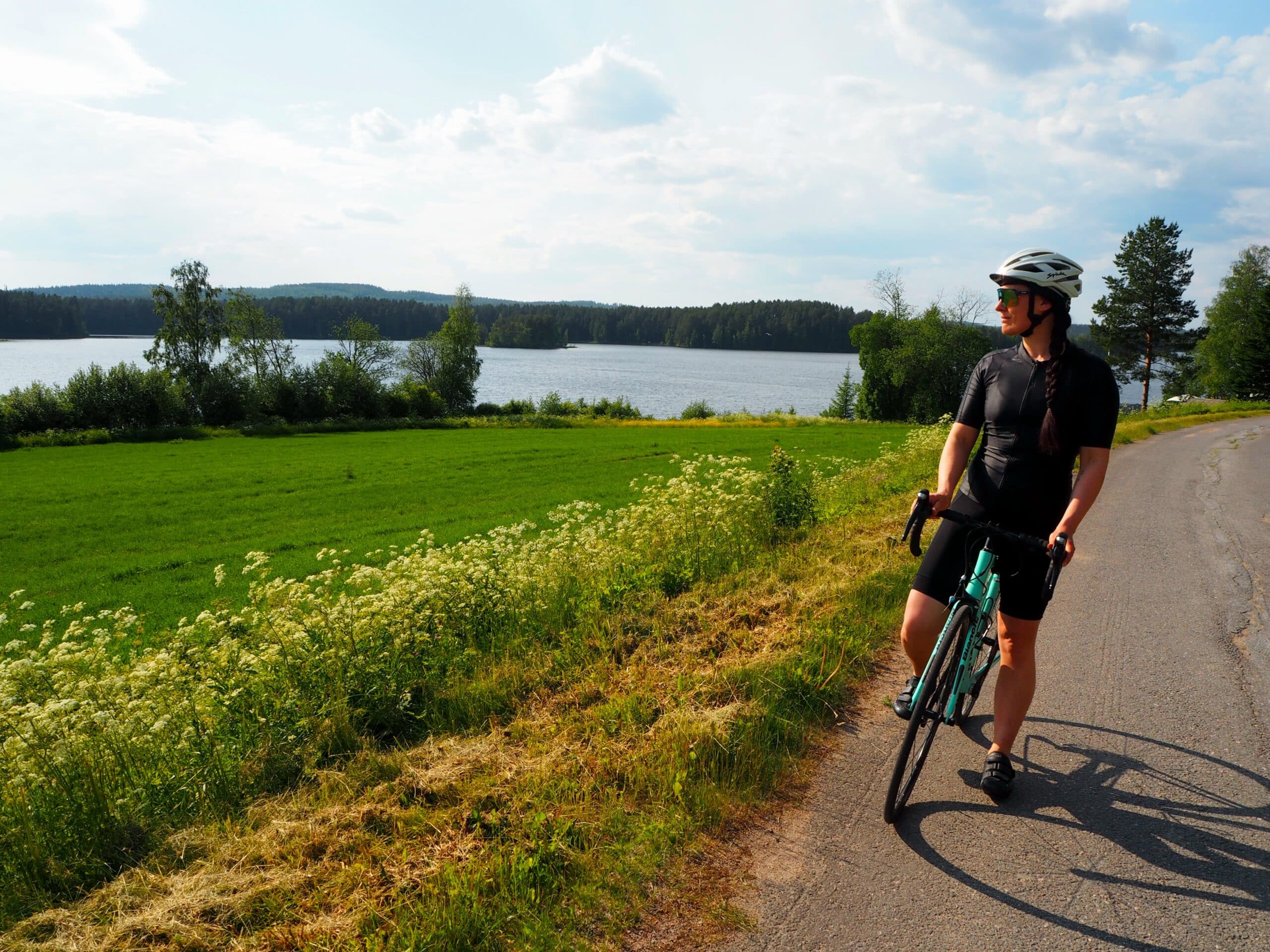 Nainen maantiepyöräilee kesällä järven läheisyydessä.