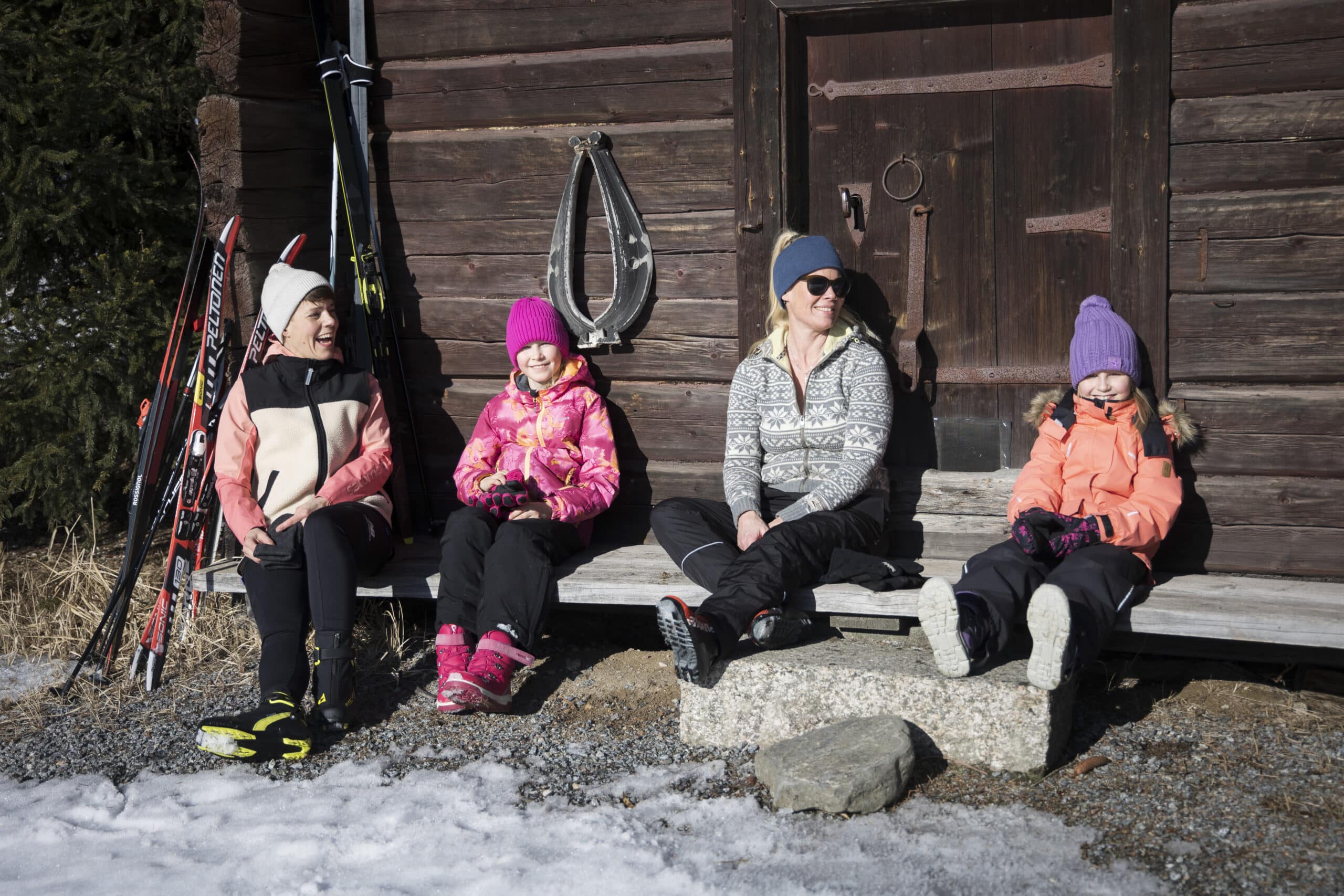Neljä hiihtäjää levähtää tuvan ulkopuolella