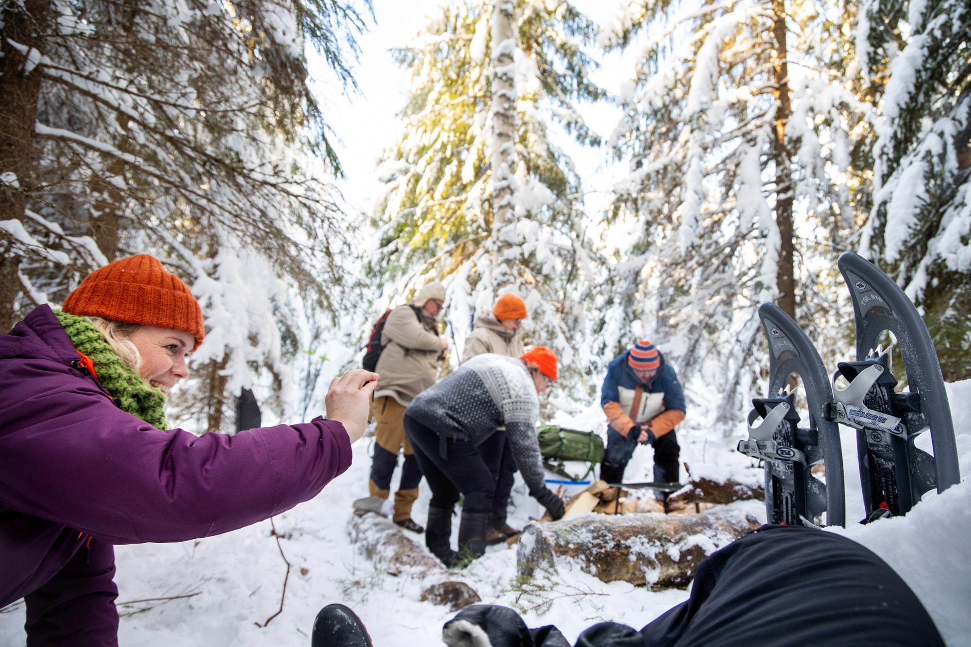 Ryhmä lumikenkäilijöitä nuotion äärellä lumisessa metsässä