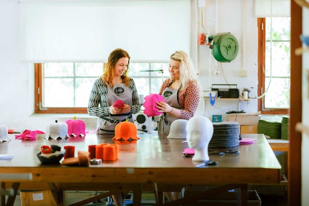 Kaksi henkilö katselee huopahattuja tehtaalla