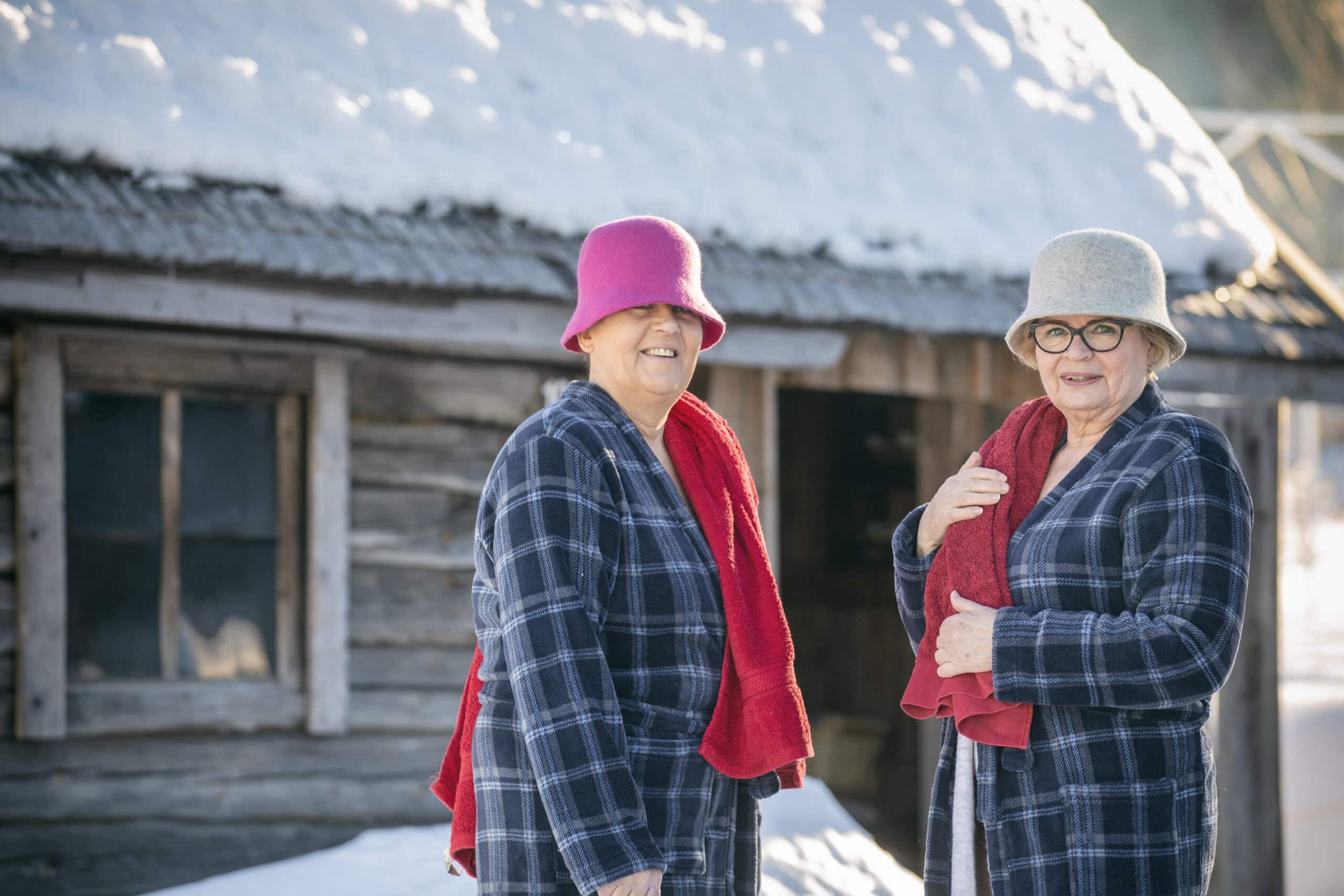 Kaksi henkilöä saunan edessä huopahatut päässä