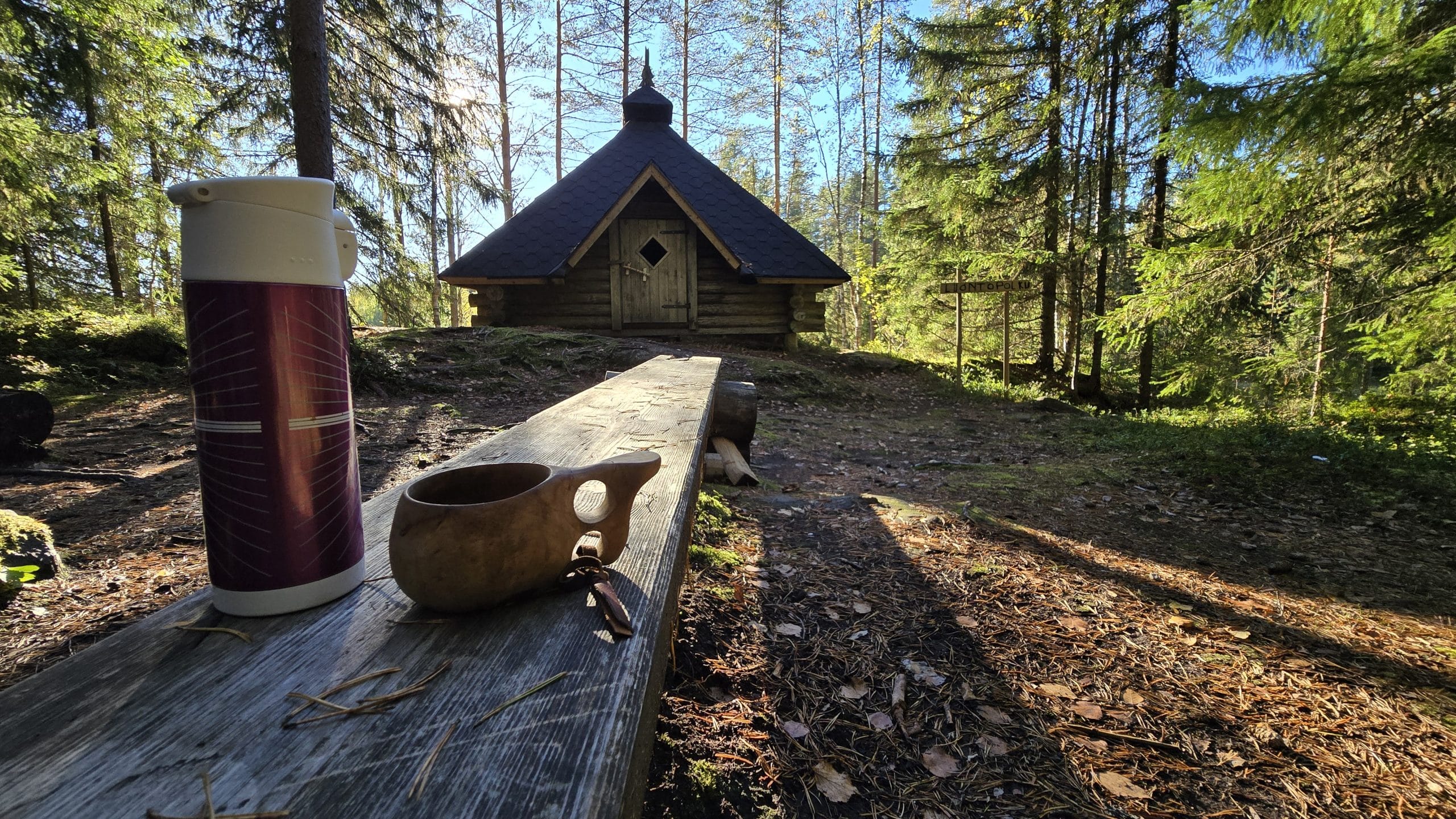 Kuksa ja termosmuki luontopolun taukopaikan puisella penkillä