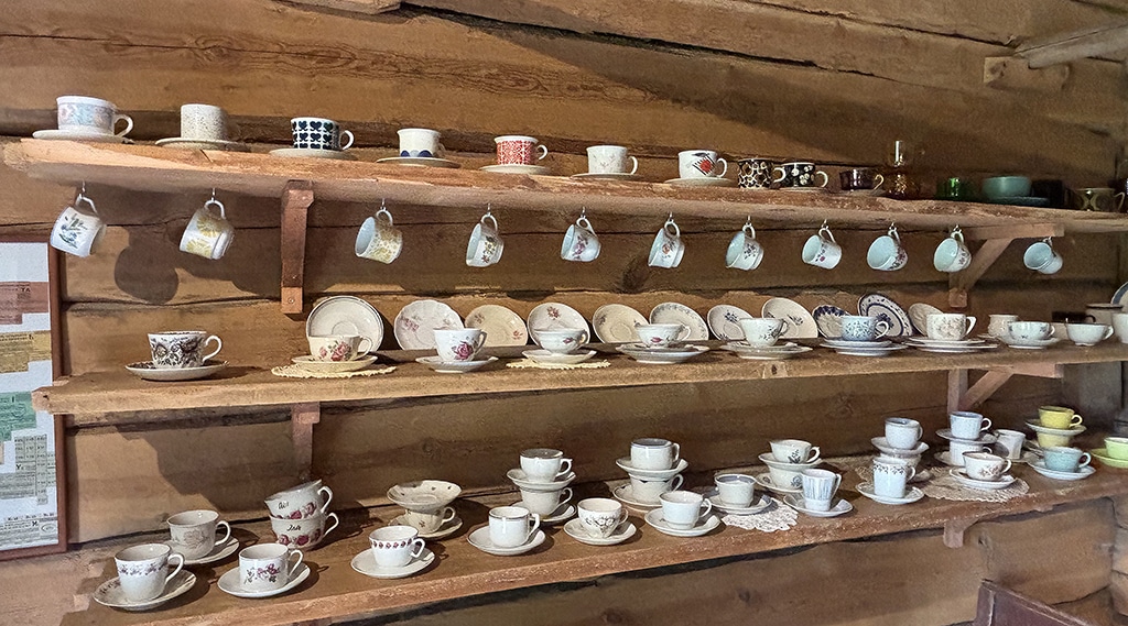 Vanha astiahylly museossa, jossa vanhoja kahvikuppeja ja aluslautasia.