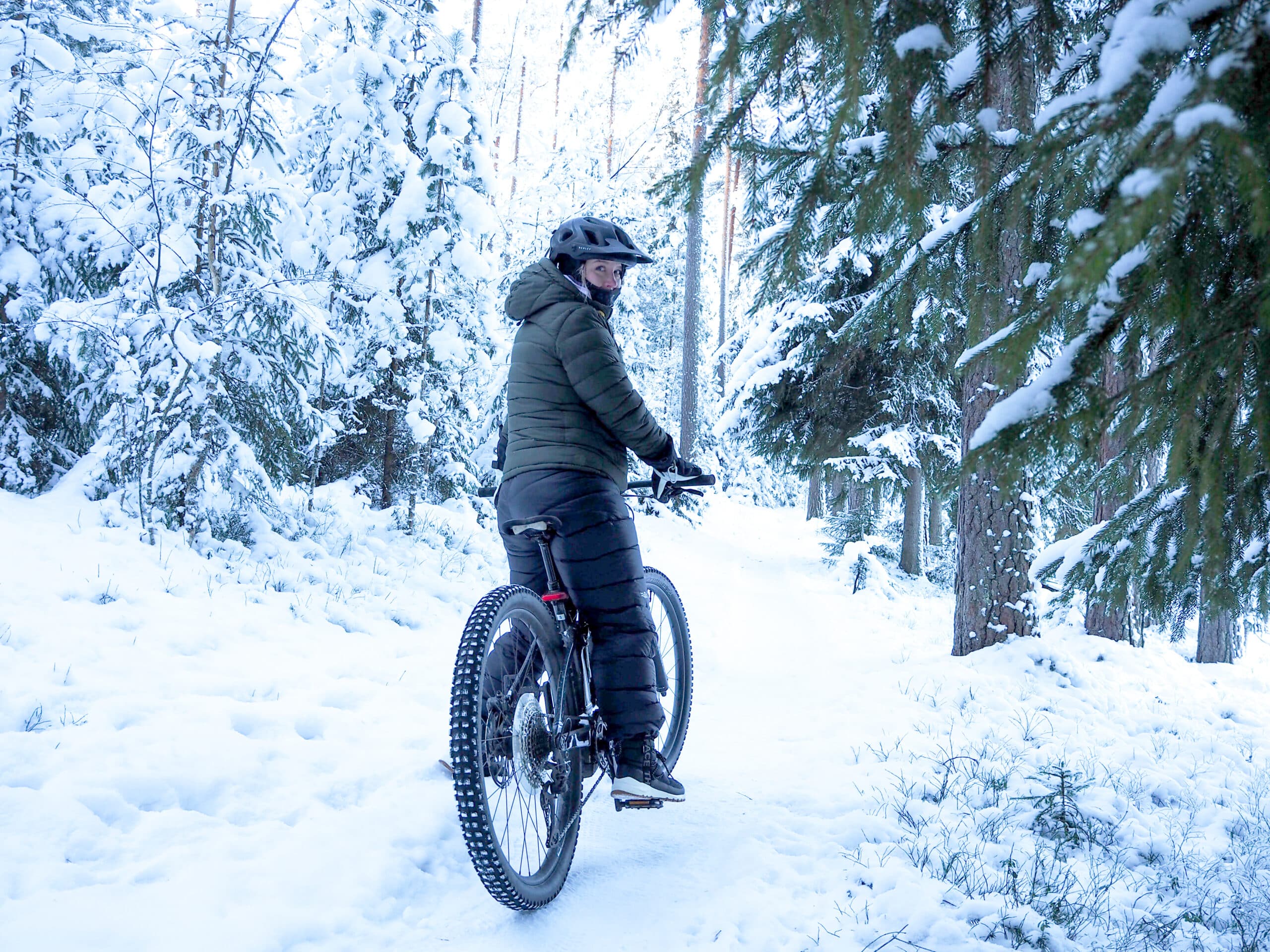 Henkilö pyöräilee lumisessa metsässä