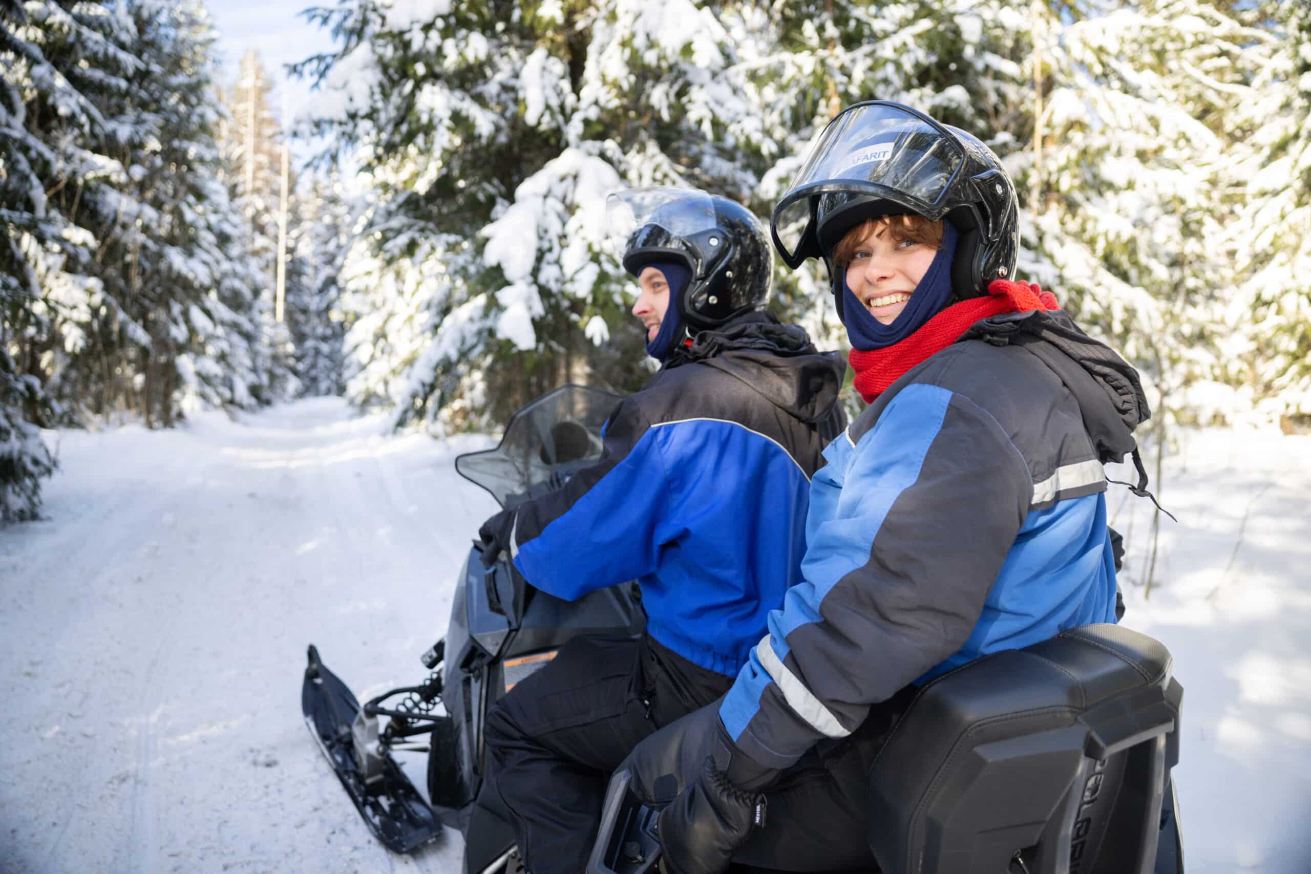 Kaksi henkilöä istuu moottorikelkan päällä metsässä