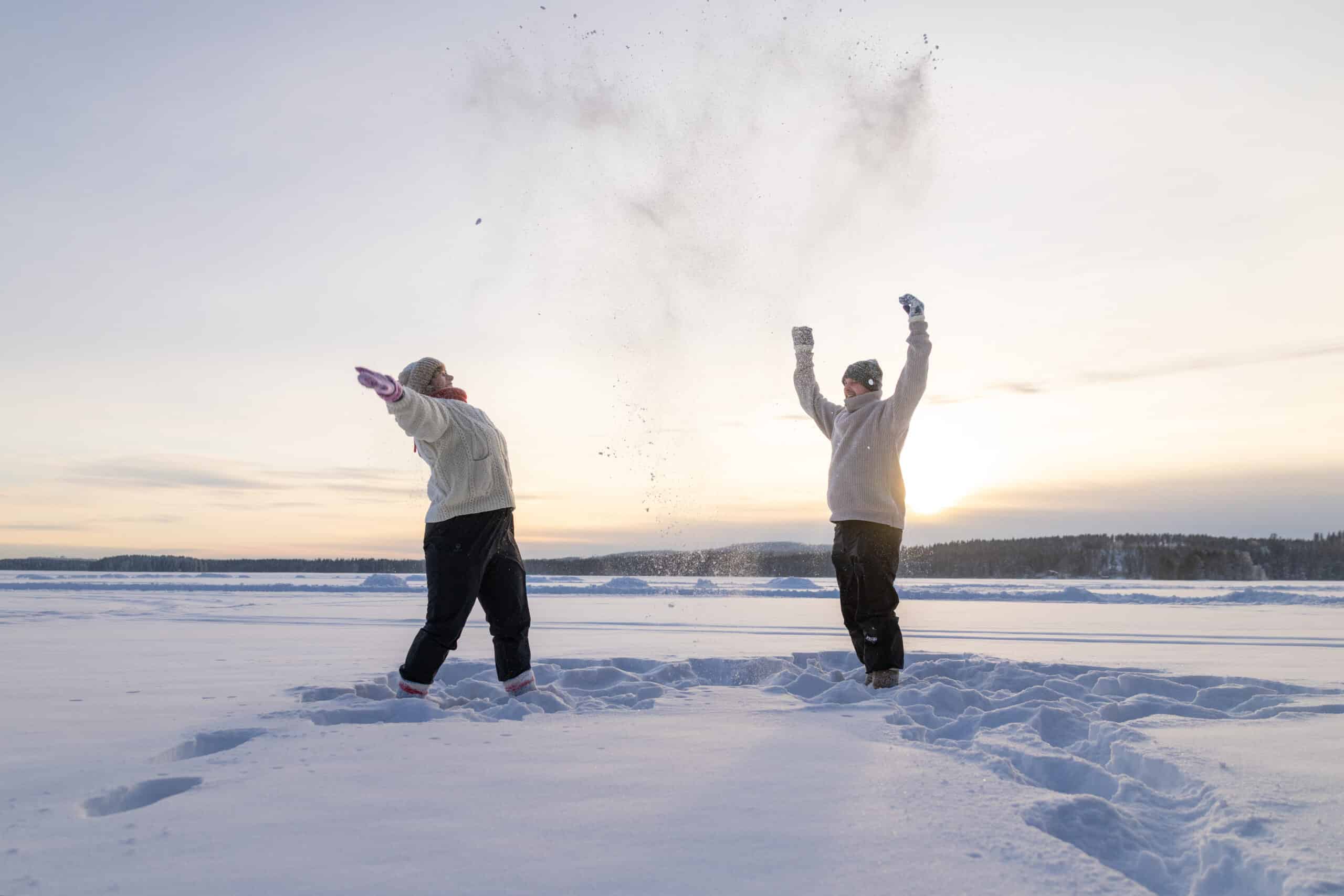 Henkilöt heittävät lunta ilmaan järven jäällä talvella